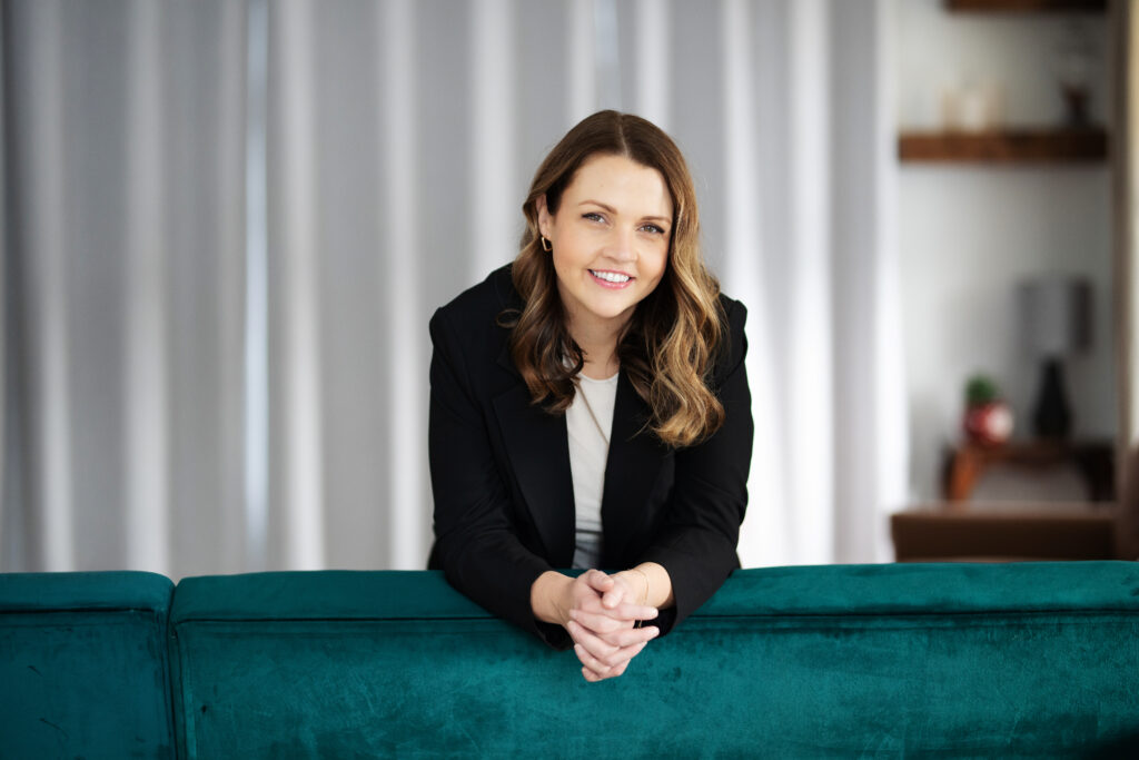 Woman leaning over green couch in a black blazer