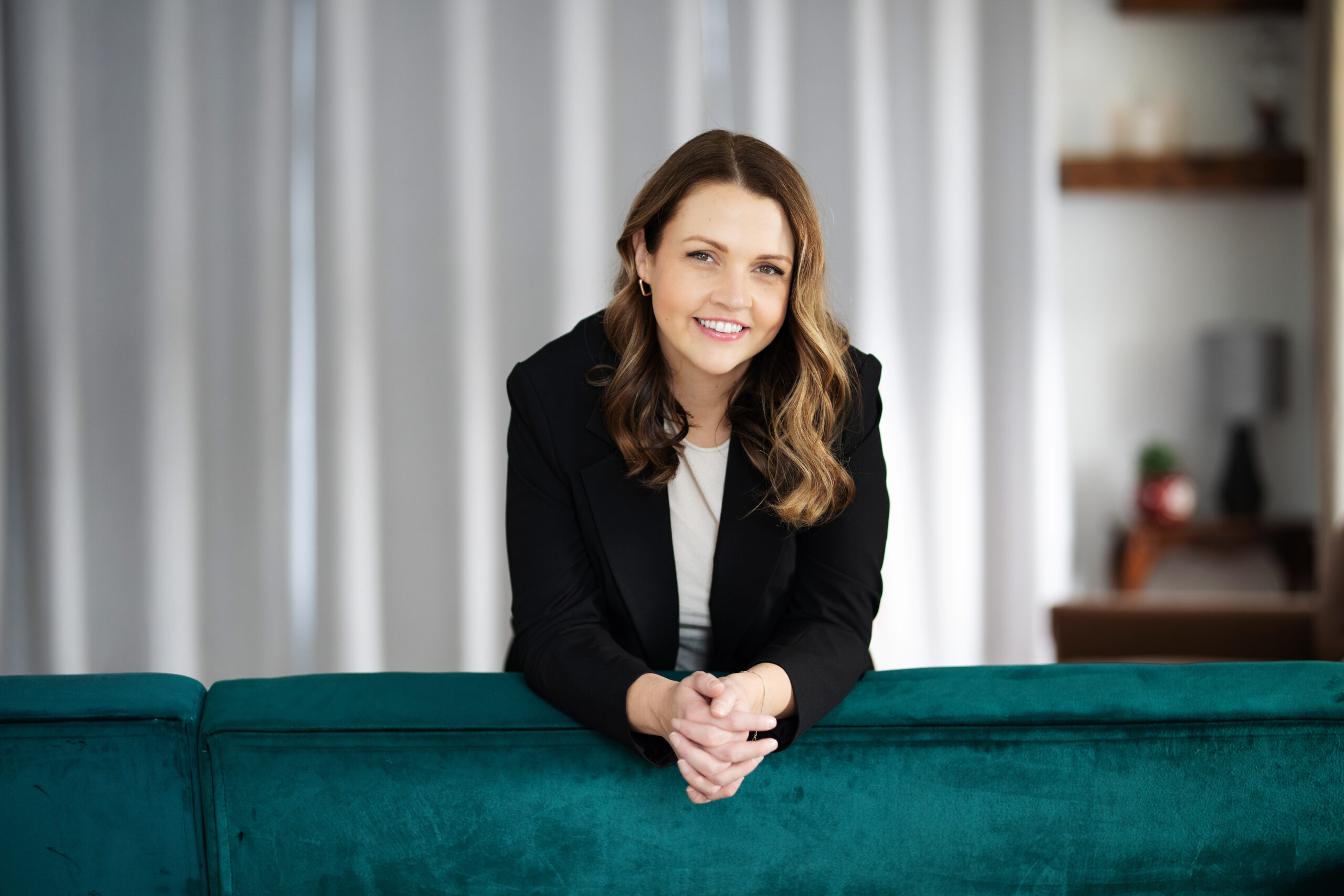 Woman wearing a blazer leaning over a green couch during a branding photo session